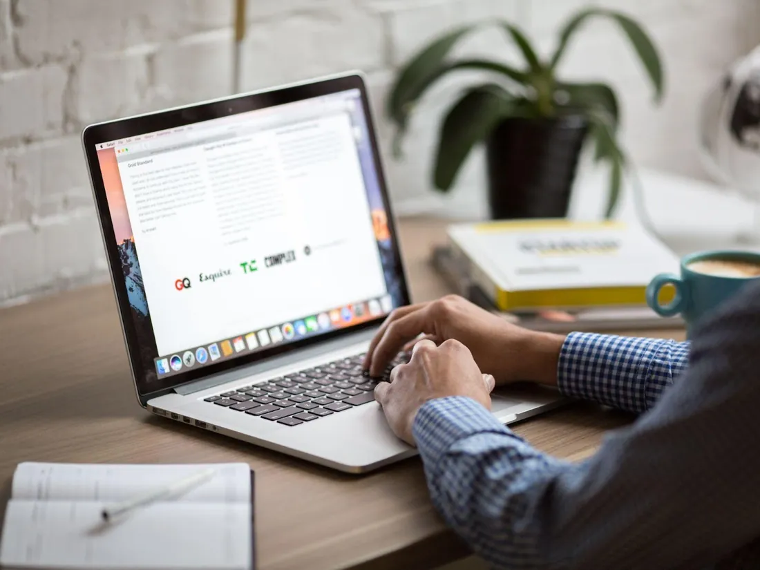 Hands typing on a MacBook at a desk