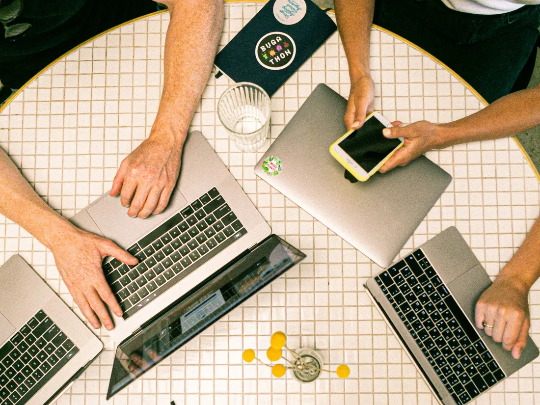 People working on MacBooks around a table, seen from above