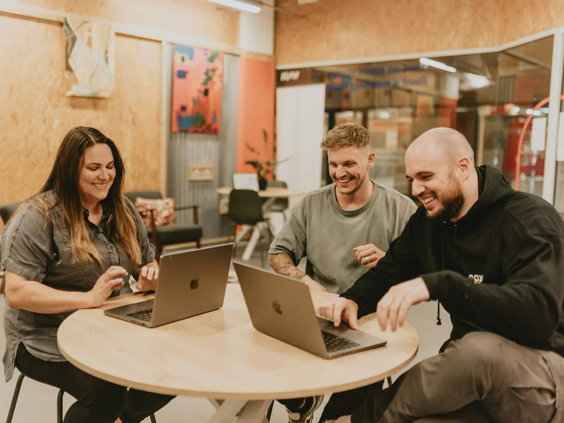 Three people working together on MacBooks at a round table